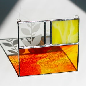 Puede incluir: Una ventana de vitral colgante con un diseño de hojas blancas, un panel amarillo y un panel rojo y naranja.