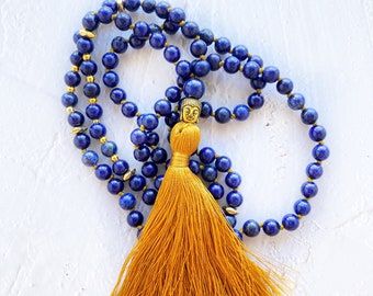 May include: A blue lapis lazuli mala with a gold Buddha charm and a yellow tassel.