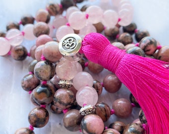 May include: A pink and brown gemstone mala with a pink tassel and a silver Om charm.
