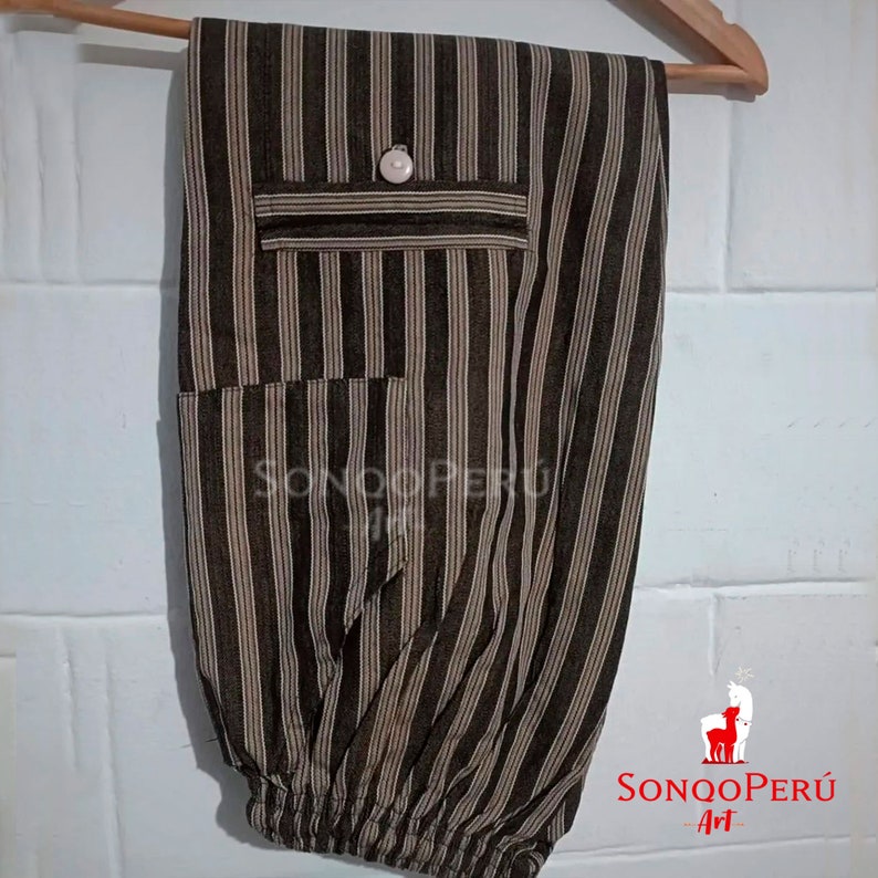 May include: Brown and beige striped pants with a button and a pocket. The pants have a drawstring at the bottom. The pants are hanging on a wooden hanger. The text "SONQO PER&Uacute; Art" is visible in the bottom right corner of the image.