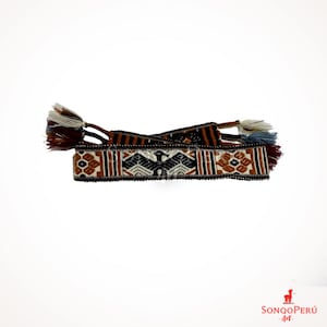 May include: A brown, black and white woven belt with a geometric pattern and a stylised bird design. The belt has tassels on each end.