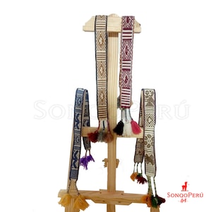 Puede incluir: Cuatro cinturones tejidos de colores con patrones geométricos y borlas colgando de un caballete de madera. Los cinturones están hechos de lana de alpaca y son una artesanía tradicional peruana.