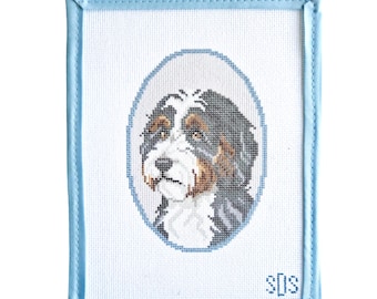 May include: A rectangular needlepoint canvas featuring a cross-stitched portrait of a tricolor dog inside a light blue oval border. The dog has black, white, and brown fur. The canvas has a light blue fabric border and the letters SDS in the corner.