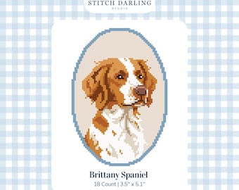 May include: A digital cross stitch pattern featuring a Brittany Spaniel portrait inside an oval frame. The text reads Stitch Darling Studio, Brittany Spaniel, 18 Count | 3.5" x 5.1", and Digital Stitch Chart. The dog has brown and white fur.