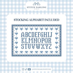 May include: A cross-stitch pattern featuring the English alphabet in a blue pixelated font, surrounded by a rectangular border of small blue hearts. The text "STOCKING ALPHABET INCLUDED" is printed above the pattern, and the logo "STITCH DARLING STUDIO" is at the top.