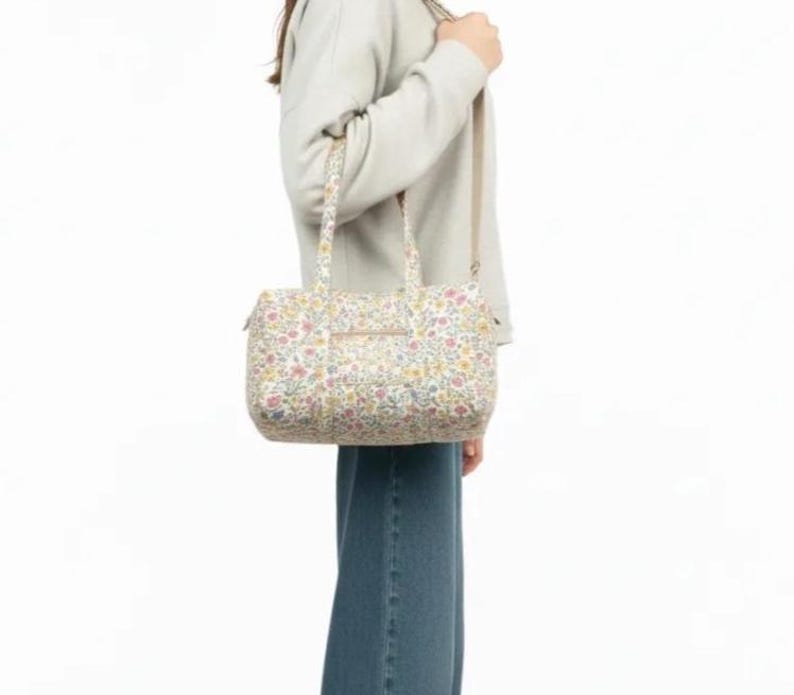 May include: A floral print handbag with a shoulder strap and top handles. The bag features a pattern of small flowers in shades of pink, yellow, and blue on a cream background. The bag is rectangular with a zipper closure.