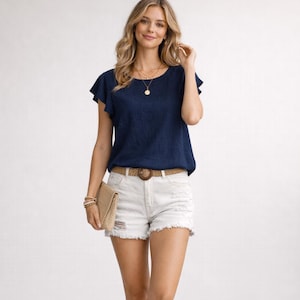 May include: A woman wearing a navy blue short-sleeved top with ruffled sleeves, paired with white distressed denim shorts. A woven belt and a tan clutch complete the outfit. The woman is also wearing gold necklaces and bracelets.