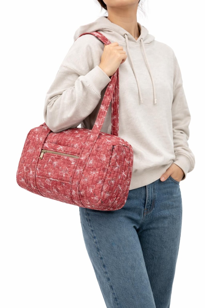 Pu&ograve; includere: Una borsa da viaggio trapuntata rossa con un motivo floreale bianco. La borsa ha una cerniera dorata e manici abbinati. La borsa viene portata a tracolla. &Egrave; una borsa da viaggio o da palestra.