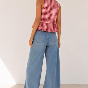 May include: A sleeveless red and white gingham peplum top paired with light blue wide-leg denim jeans and white sneakers. The top features a square neckline and a ruffled hem, while the jeans have a classic five-pocket design and a loose fit.