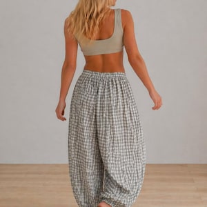 May include: A light beige crop top and gray and white checkered pants. The pants have a loose, gathered design. The model is wearing black sandals. The outfit is casual and comfortable.