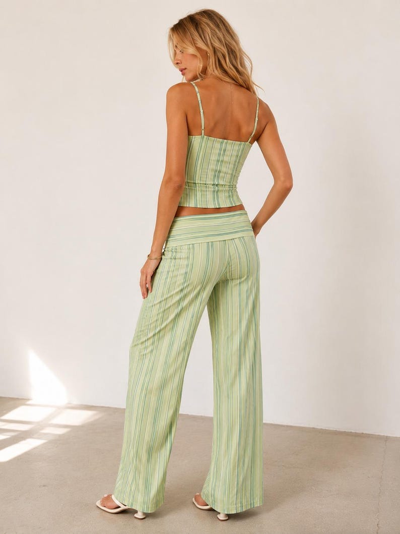 May include: A two-piece outfit featuring a striped camisole top and matching wide-leg pants. The set is in shades of green and white, with vertical stripes. The top has thin straps, and the pants have a high waist. The outfit is made of a lightweight fabric.