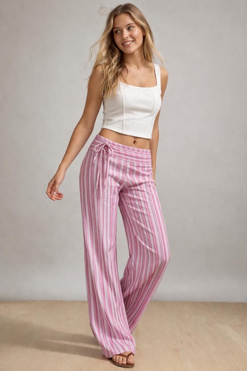 May include: A woman wearing a white crop top and pink and white striped palazzo pants. The pants have a drawstring waist. The outfit is casual and summery.