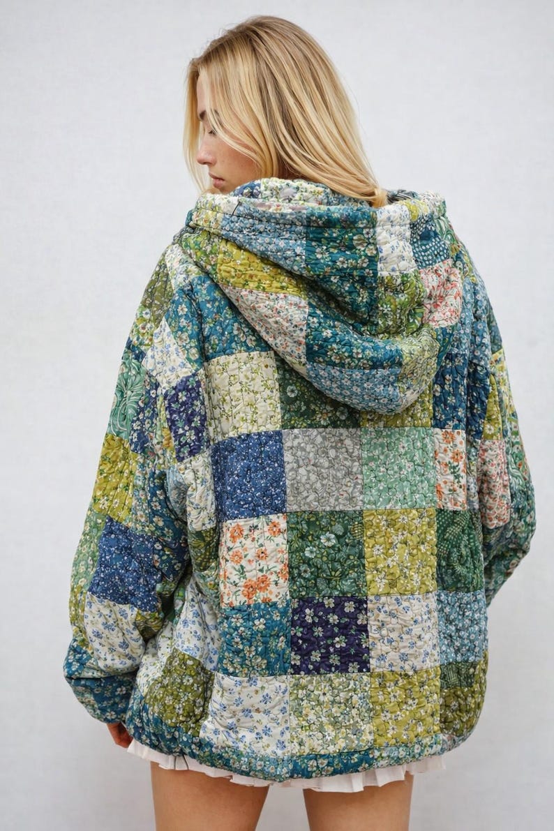 May include: A quilted hoodie jacket with a patchwork design. The jacket features a variety of floral patterns in shades of blue, green, and orange. The jacket has a hood and a relaxed fit, perfect for layering.