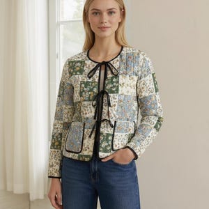 Może przedstawiać: Pikowana kurtka z patchworkowym wzorem z kwiatowymi wzorami w kolorze zielonym, niebieskim i kremowym. Kurtka ma czarne wykończenie, dwie kieszenie i czarne wiązanie. Rękawy są długie, a kurtka jest noszona otwarta.