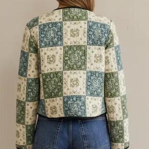 Może przedstawiać: Pikowana kurtka z patchworkowym wzorem. Kurtka ma kwadratowy wz&oacute;r w odcieniach zieleni, błękitu i kremu, z czarnym wykończeniem. Ubranie jest noszone z niebieskimi dżinsami.