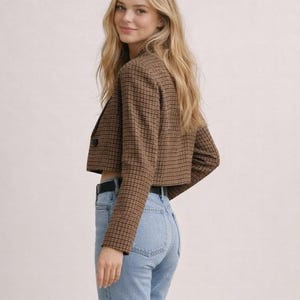 May include: Cropped brown plaid blazer with a single button closure. The blazer is paired with light wash blue jeans and a black belt. The outfit is a classic and stylish combination.