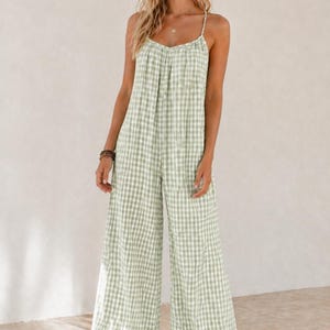 May include: A light green and white gingham-patterned jumpsuit with wide legs and spaghetti straps. The jumpsuit is made of a lightweight fabric, suitable for warm weather. The model is wearing sandals.