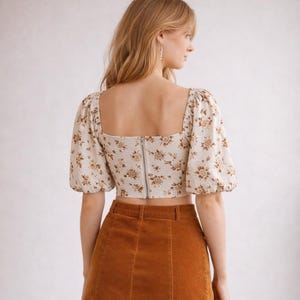 Peut inclure: Un haut court cr&egrave;me &agrave; motifs floraux et manches bouffantes est associ&eacute; &agrave; une jupe en velours c&ocirc;tel&eacute; marron. Le haut a une encolure carr&eacute;e et une fermeture &eacute;clair dans le dos. La jupe a une taille haute et une fermeture boutonn&eacute;e.