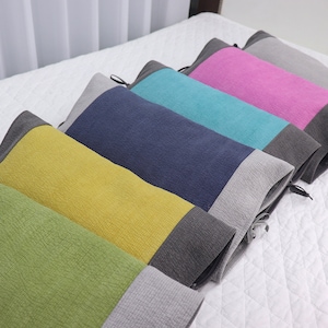 May include: Five decorative pillows with a two-tone design. The pillows are arranged in a row on a white bedspread. The pillows are green, yellow, blue, turquoise, and pink. Each pillow has a gray band at the bottom.