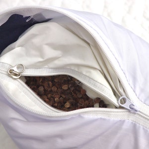May include: A white pillow with a zipper opening, revealing a buckwheat hull filling. The pillow has a blue and white patterned fabric on the outside.