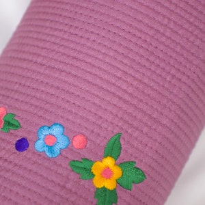K&ouml;nnte beinhalten: Ein lila gestepptes Kissen mit gestickten Blumen in den Farben Rosa, Blau, Gelb und Gr&uuml;n.