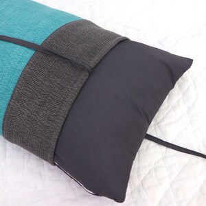 May include: A long teal and gray pillow with a black tie closure. The pillow is lying on a white surface.