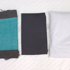 May include: Three rectangular pillows, one teal with a gray border, one dark gray, and one white.