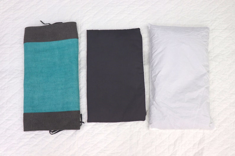 May include: Three rectangular pillows, one teal with a gray border, one dark gray, and one white.