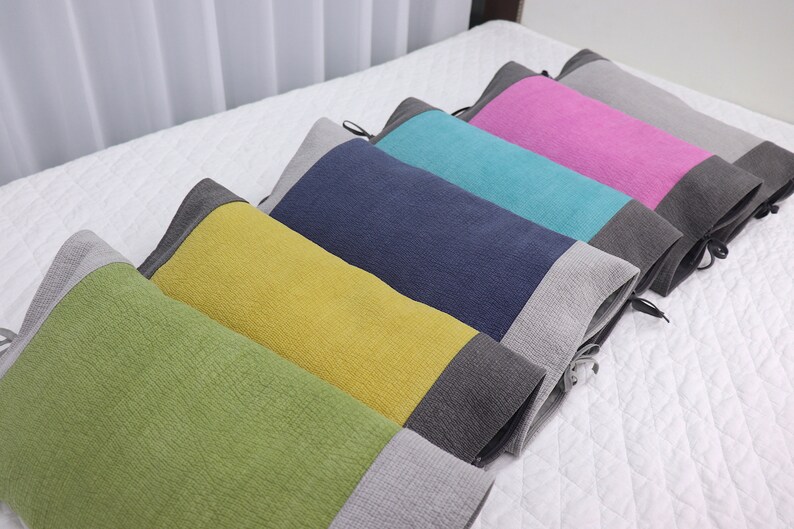 May include: Five decorative pillows with a two-tone design. The pillows are arranged in a row on a white bedspread. The pillows are green, yellow, blue, turquoise, and pink. Each pillow has a gray band at the bottom.