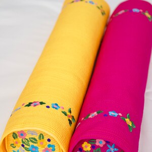 K&ouml;nnte beinhalten: Zwei zylindrische Kissen mit Blumenstickerei. Ein Kissen ist gelb mit blauen und rosa Blumen, das andere ist rosa mit gelben, blauen und rosa Blumen.