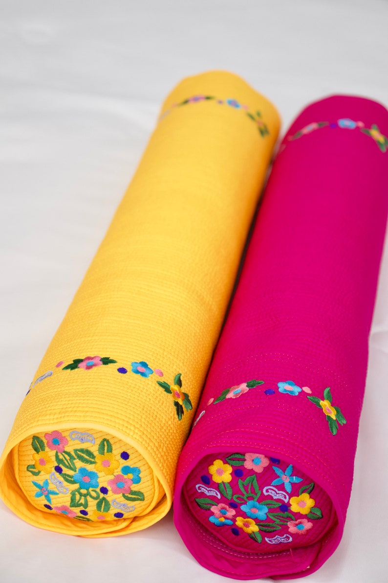 K&ouml;nnte beinhalten: Zwei zylindrische Kissen mit Blumenstickerei. Ein Kissen ist gelb mit blauen und rosa Blumen, das andere ist rosa mit gelben, blauen und rosa Blumen.