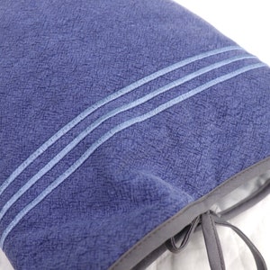 May include: A blue fabric pouch with a drawstring closure and two white stitching lines. The pouch is made of a textured fabric.