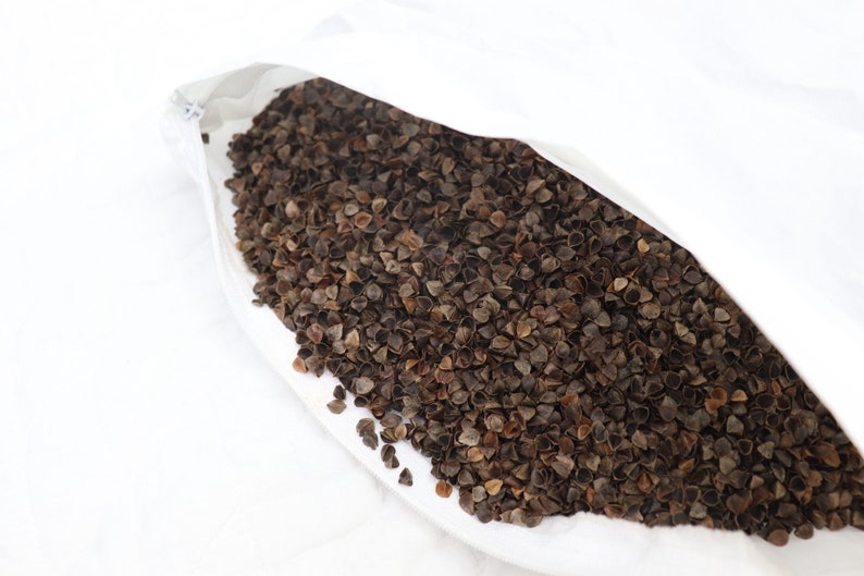 May include: A white pillowcase filled with buckwheat hulls. The hulls are brown and have a slightly irregular shape.