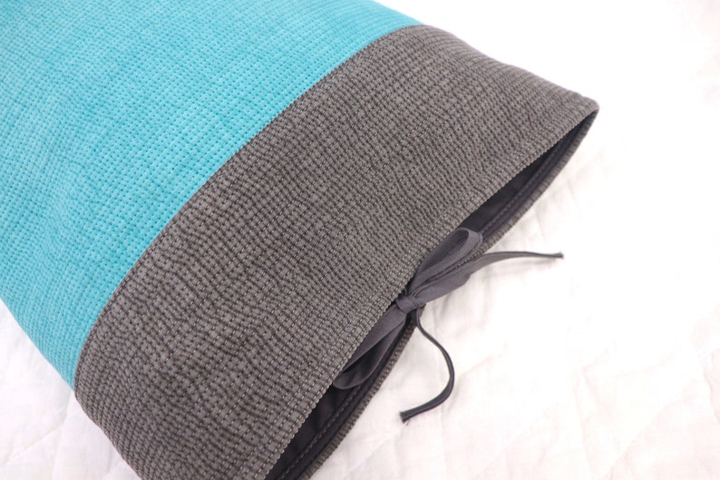 May include: A turquoise and gray pillow with a drawstring closure. The pillow is made of a soft, textured fabric.