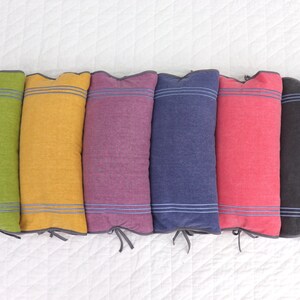 May include: Six decorative pillows with different colored fabric and a white stripe design. The pillows are arranged in a row on a white surface.