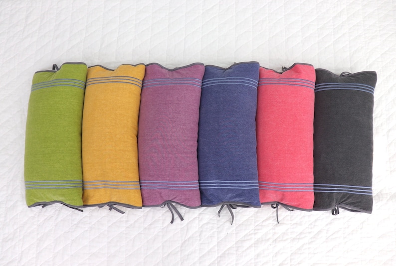 May include: Six decorative pillows with different colored fabric and a white stripe design. The pillows are arranged in a row on a white surface.