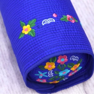 K&ouml;nnte beinhalten: Ein blaues, zylindrisches Kissen mit gestickten Blumen in Gelb-, Rosa-, Blau- und Gr&uuml;nt&ouml;nen.