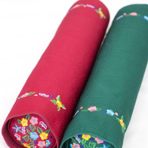 K&ouml;nnte beinhalten: Zwei zylindrische Kissen mit gestickten Blumenmustern. Ein Kissen ist rot mit einem blauen und gelben Blumendesign, das andere ist gr&uuml;n mit einem gelben und blauen Blumendesign.