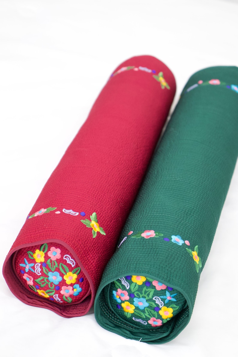 K&ouml;nnte beinhalten: Zwei zylindrische Kissen mit gestickten Blumenmustern. Ein Kissen ist rot mit einem blauen und gelben Blumendesign, das andere ist gr&uuml;n mit einem gelben und blauen Blumendesign.