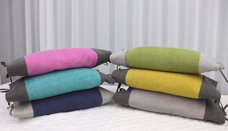 May include: Stack of four colorful cushions with gray trim. The cushions are pink, teal, navy blue, and gray.