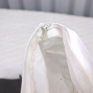 May include: A white zippered pouch with a white zipper pull. The pouch is open and the inside is visible.