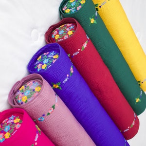K&ouml;nnte beinhalten: Ein Set aus sieben bunten zylindrischen Kissen mit gestickten Blumenmustern. Die Kissen sind in einem Stapel angeordnet, wobei das gr&ouml;&szlig;te unten und das kleinste oben liegt. Die Farben der Kissen sind gelb, gr&uuml;n, rot, blau, rosa und lila.