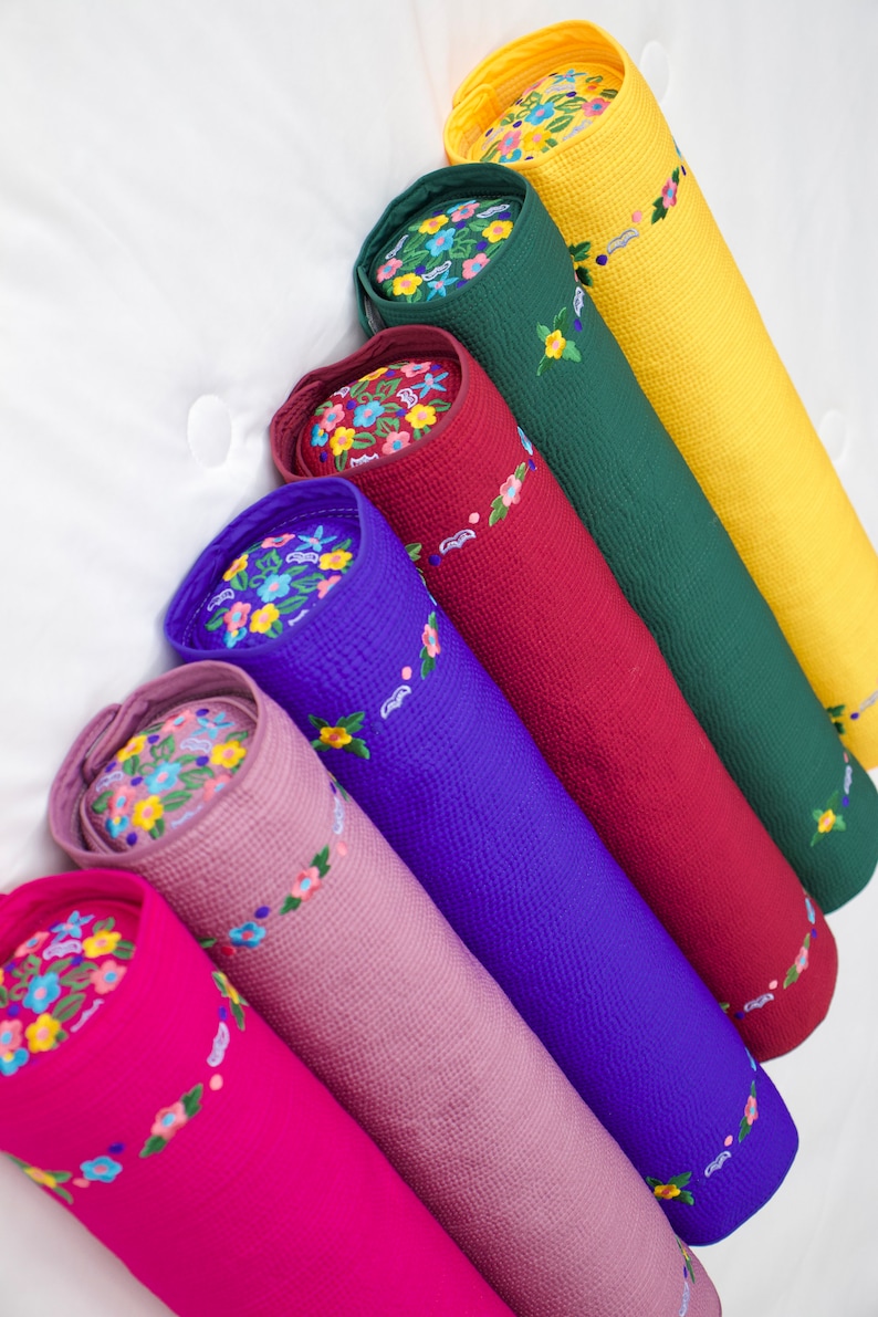 K&ouml;nnte beinhalten: Ein Set aus sieben bunten zylindrischen Kissen mit gestickten Blumenmustern. Die Kissen sind in einem Stapel angeordnet, wobei das gr&ouml;&szlig;te unten und das kleinste oben liegt. Die Farben der Kissen sind gelb, gr&uuml;n, rot, blau, rosa und lila.