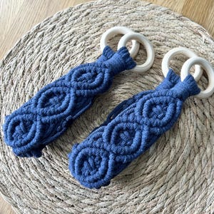 May include: Two blue macrame teardrop-shaped wall hangings with wooden rings. The macrame is made with a diamond pattern.