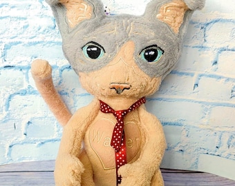 May include: A plush toy resembling a Sphynx cat with beige fur, a grey head, and large dark eyes. It features a red ribbon with white polka dots tied around its neck and a heart-shaped patch on its chest with the embroidered name Walter.
