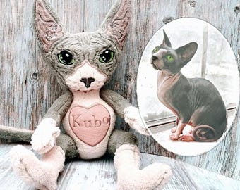 May include: A plush gray Sphynx cat doll with large green eyes, a pink heart-shaped patch with the name "Kubo", and a matching image of a real Sphynx cat. The doll has a soft, textured appearance.