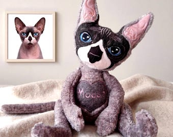 May include: A plush toy resembling a Sphynx cat with grey textured fur, large pointed ears, and blue eyes. The face features a black and white mask pattern. A dark grey heart patch on the chest displays the embroidered text Mouse in pink thread.