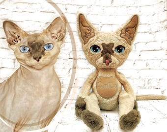 May include: A plush toy cat with tan fur, dark brown paws, and a dark brown face mask, featuring large blue eyes and a pink nose. A circular patch on the chest displays the embroidered text CoCo. The toy is shown next to a photo of a real cat.