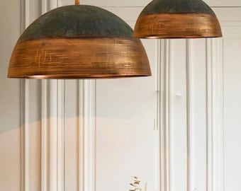 May include: Two copper and green dome-shaped pendant lights hanging from the ceiling. The larger light has a copper bottom and a green top. The smaller light has a copper top and bottom.