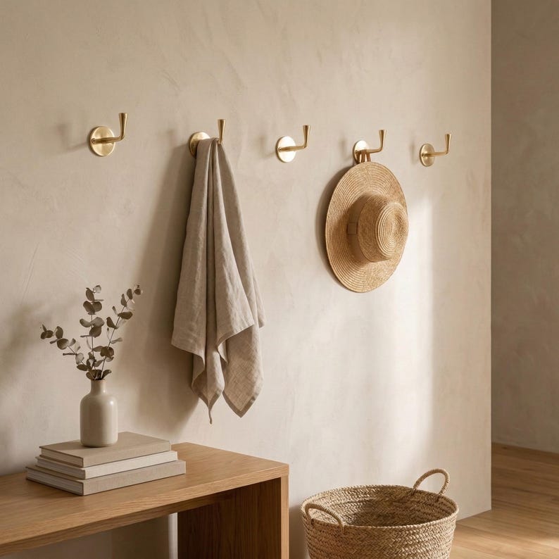Peut inclure: Int&eacute;rieur aux tons neutres avec quatre crochets muraux en laiton, une serviette beige et un chapeau de paille. Un petit vase avec de la verdure et une pile de livres sont pos&eacute;s sur une console en bois. Un panier tress&eacute; est au sol.